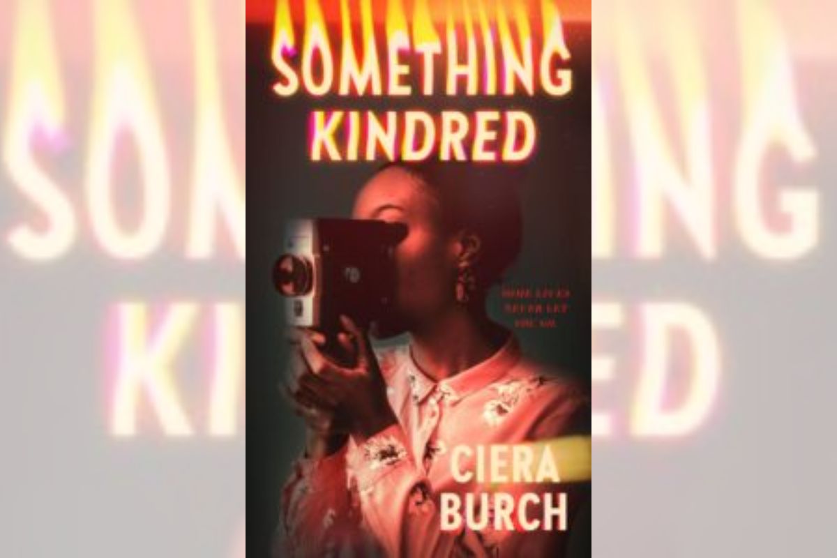 Book cover for "Something Kindred" with a woman holding an old recording camera.