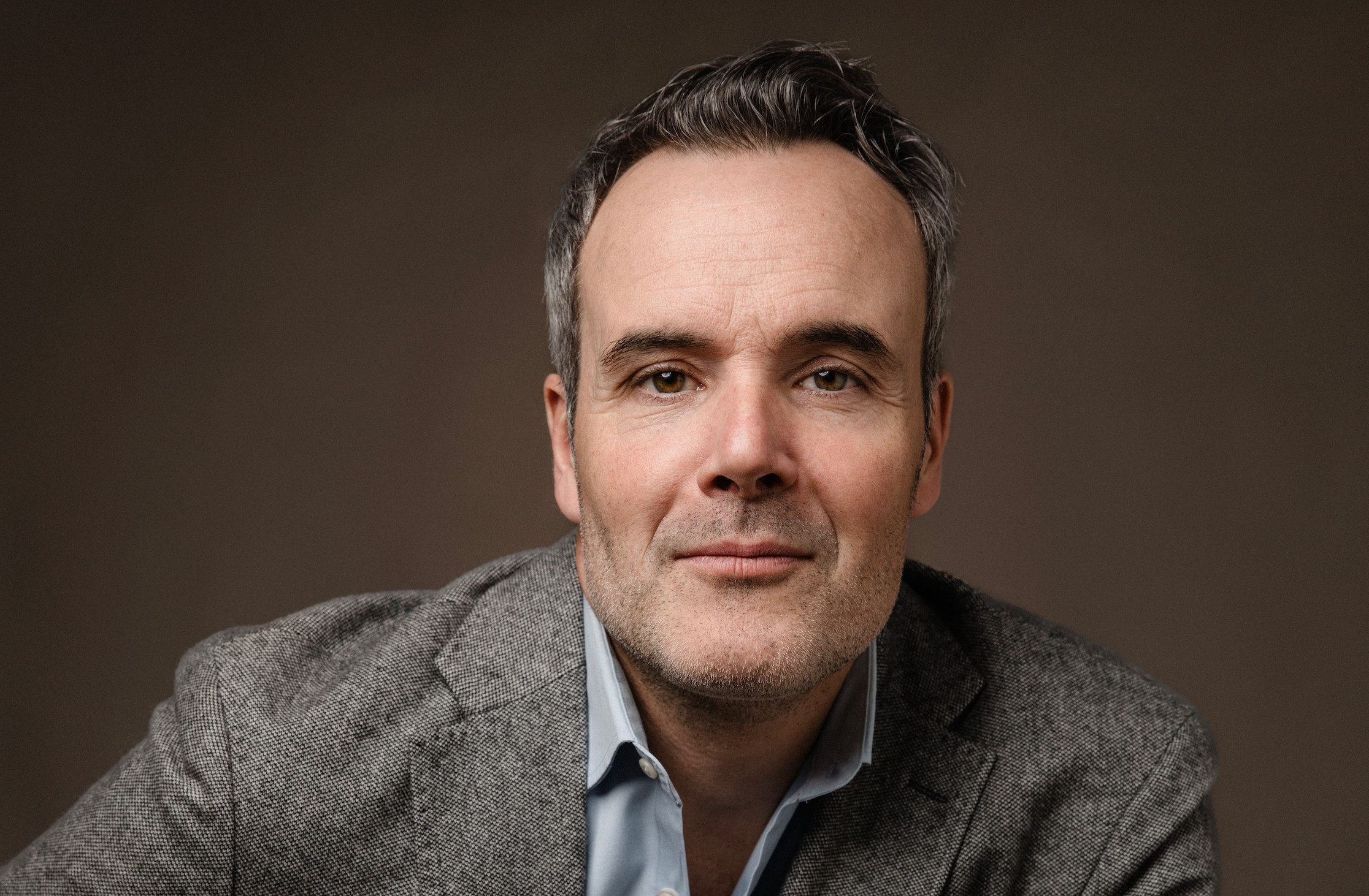 Saint-Pierre: Jean-Michel Le Gal Talks Season 2 Actor Jean-Michel Le Gal poses for a professional headshot on a brown backdrop.