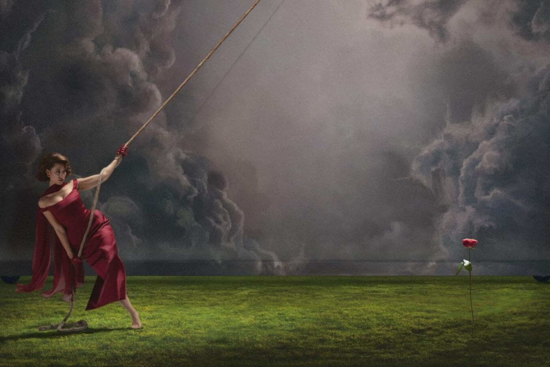 Raye’s ‘This Music May Contain Hope’ Album Review: An Emotional New Must-Listen RAYE stands in a grassy field under dramatic storm clouds, holding a long rope while a single red flower blooms nearby