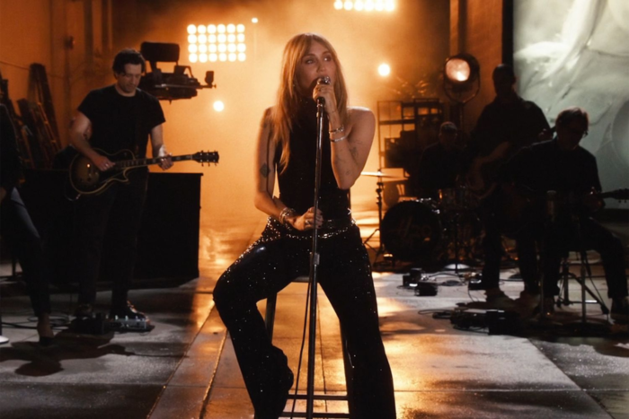 Hannah Montana 20th Anniversary Special Review: Miley Cyrus Brings Fans Back to Where It All Began Miley Cyrus performing on stage with a microphone and band under warm stage lighting