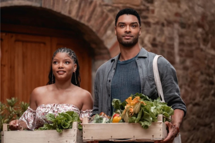Halle Bailey and Regé-Jean Page carry a crate of fresh vegetables through a rustic Italian village