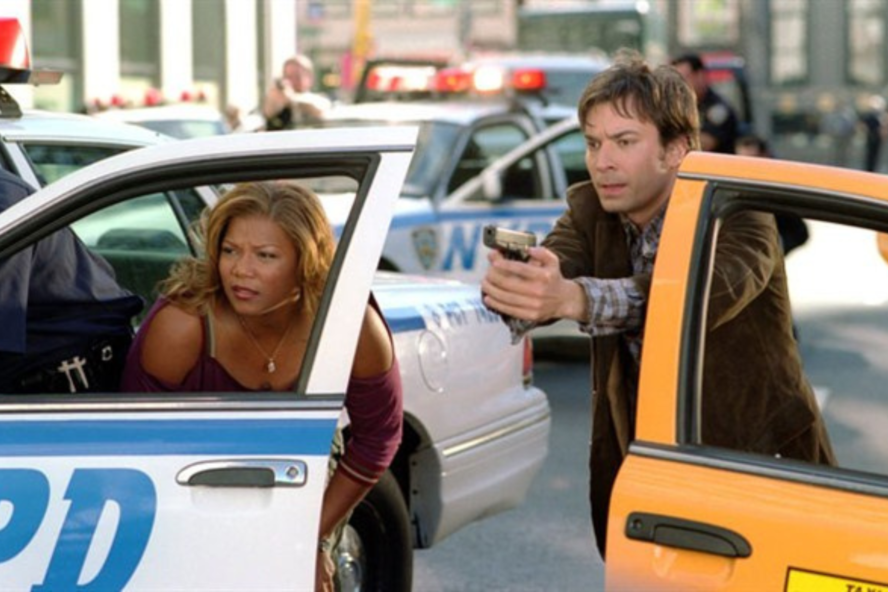Queen Latifah as Belle Williams crouching behind a police car during a chase in Taxi