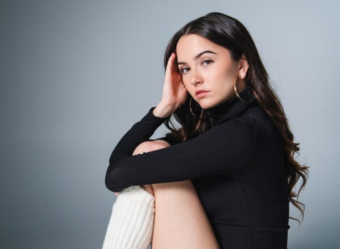 Hannah Cheramy Talks FROM Season 4 and Julie’s Journey Actress Hannah Cheramy, who stars in FROM Season 4, poses for a professional headshot while wearing a black leotard with white leggings. She sits in front of a gray backdrop.