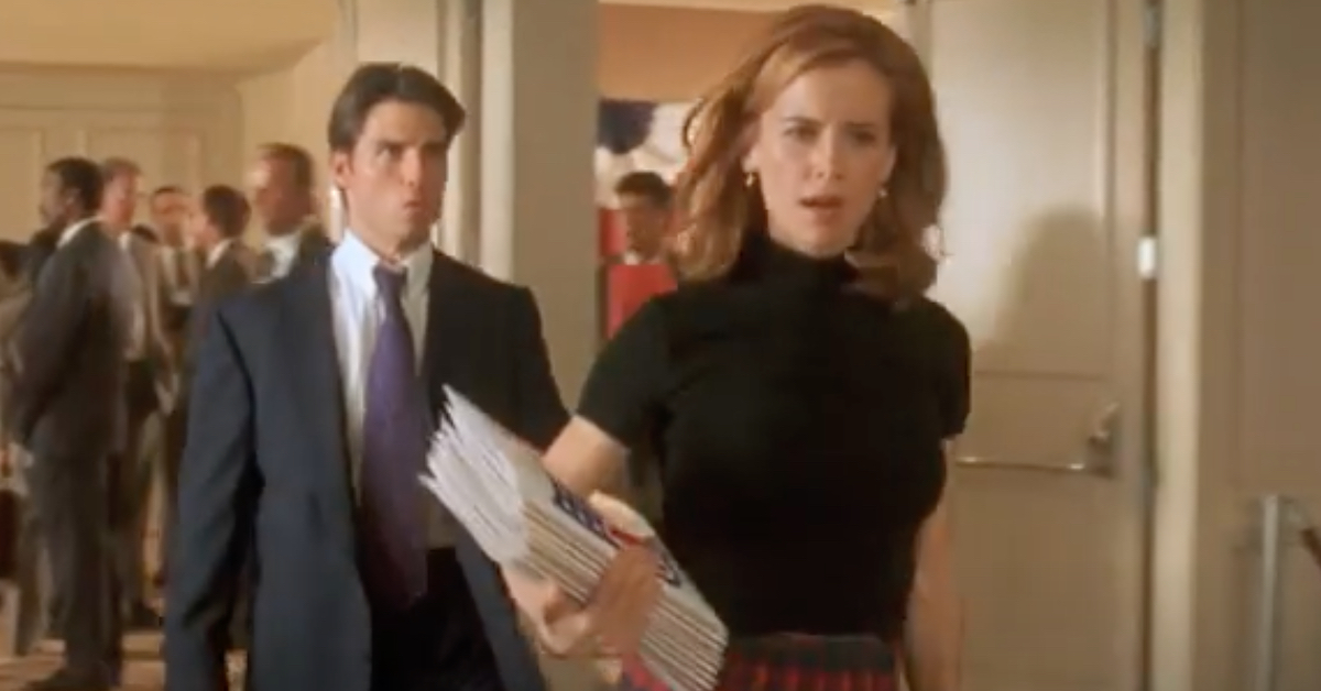 Jerry Maguire 30th Anniversary Review: Tom Cruise’s Most Heartfelt Work Still Holds Up Woman in a black top carries a stack of papers as she walks down a hallway, with a suited man following behind.