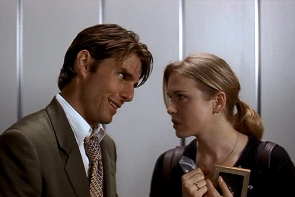 Tom Cruise and Renee Zellweger in Jerry Maguire. Man in a suit leans close to a woman in an elevator, both looking at each other; she holds a notebook and folder and appears surprised.