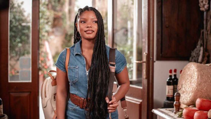 Halle Bailey as Anna stands inside a rustic Italian home with a backpack, looking hopeful and curious