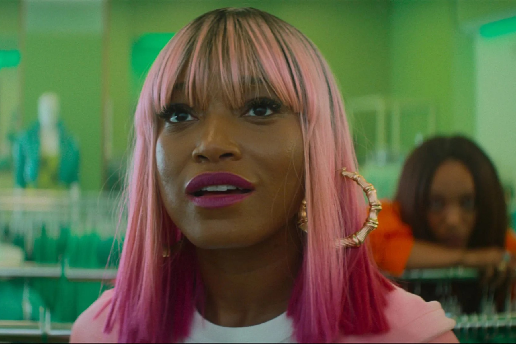 I Love Boosters Review: Stylish, Strange, and Slightly Uneven Keke Palmer wears a bright pink wig and large hoop earrings while reacting with surprise inside a clothing store.