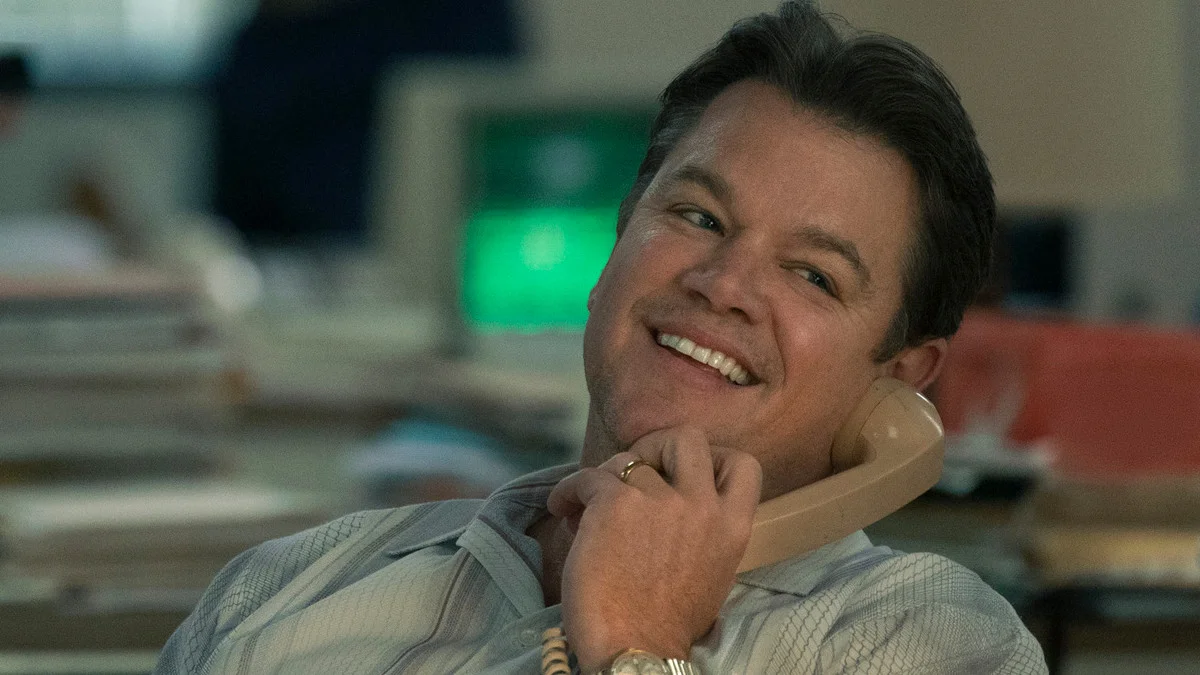 The 12 Best Movies Featuring Matt Damon in a Principal Role Smiling man in a business shirt talking on a beige landline phone at his desk in an office.