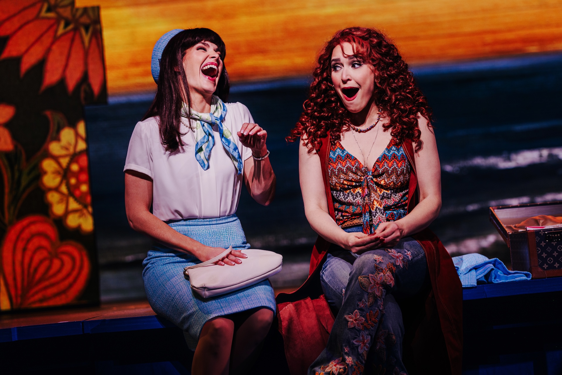 Beaches: A New Musical Review: A Beautiful Tale of Friendship Told in a Heartwarming Fashion Two women on a colorful stage share a laugh during a performance, seated side by side.