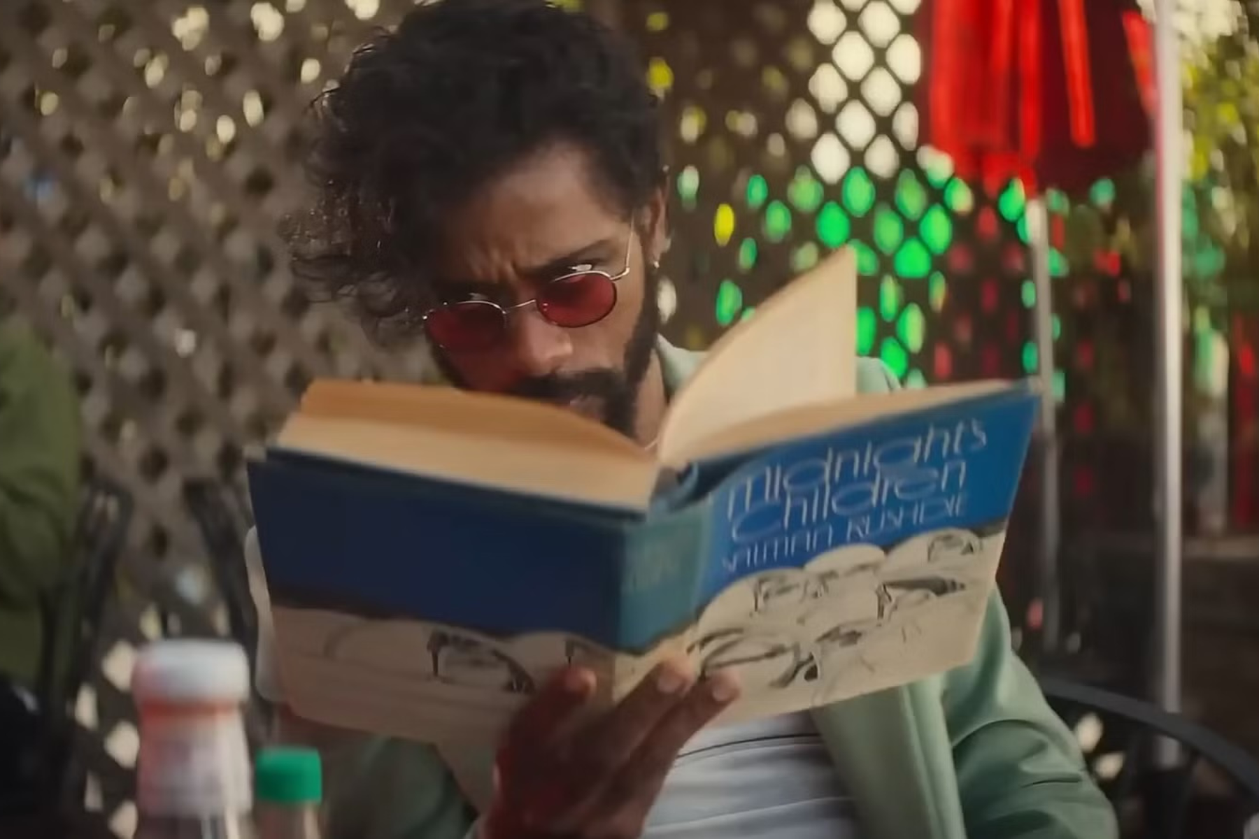 I Love Boosters Review: Stylish, Strange, and Slightly Uneven LaKeith Stanfield reads a large blue book while wearing tinted sunglasses and a light green jacket in a scene from I Love Boosters.