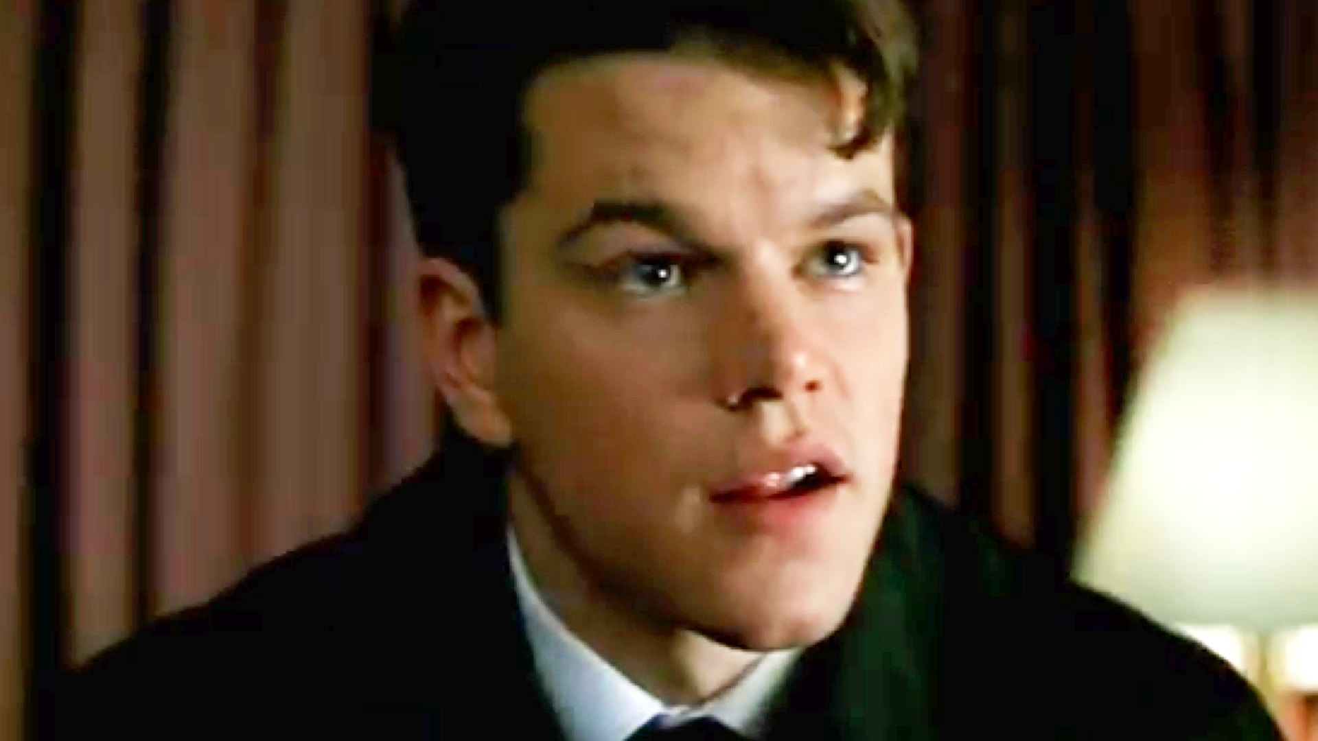 The 12 Best Movies Featuring Matt Damon in a Principal Role Close-up of a young man in a suit looking to the right in a dim room.