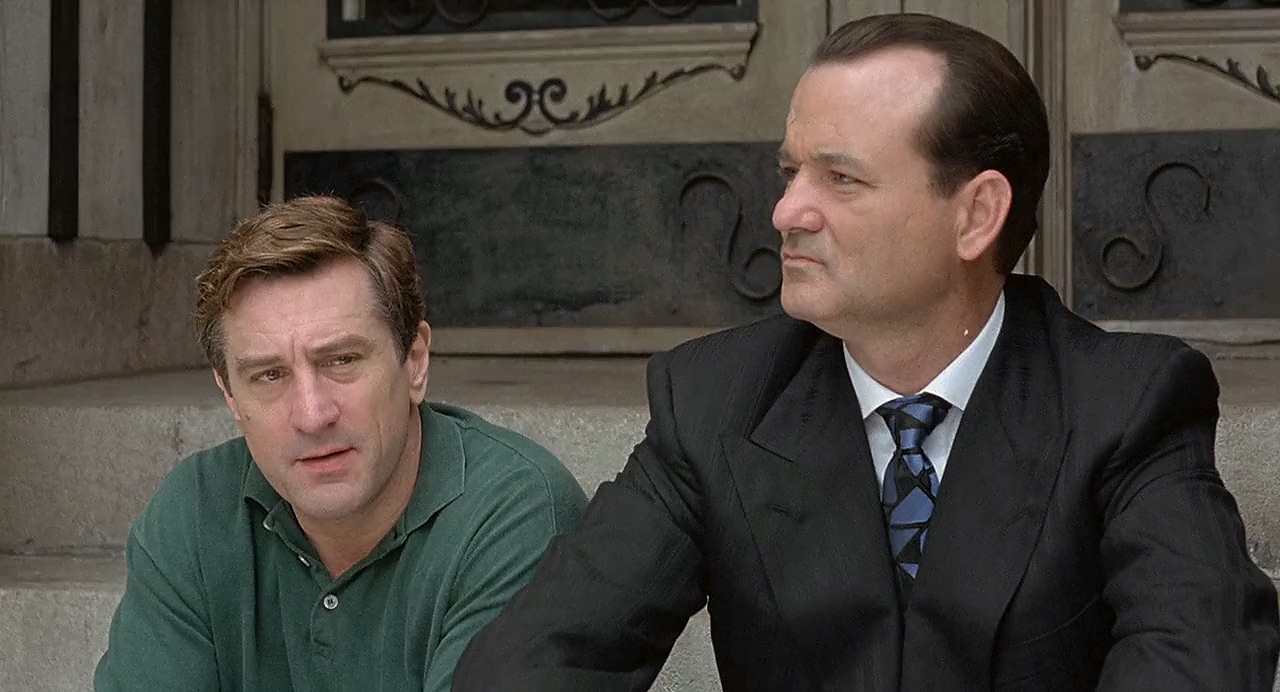 The 12 Greatest Movies Featuring Bill Murray Two men sit on stone steps outside a building; the man in a green polo looks concerned while the man in a dark suit gazes to the right.