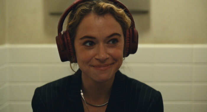 Maximum_Pleasure_Guaranteed_Photo_010107 - Eulalie Magazine Maximum Pleasure Guaranteed Season 1 Episode 1 and 2 Review: Magnets / YABA Woman wearing red over-ear headphones, smiling softly in an indoor setting.