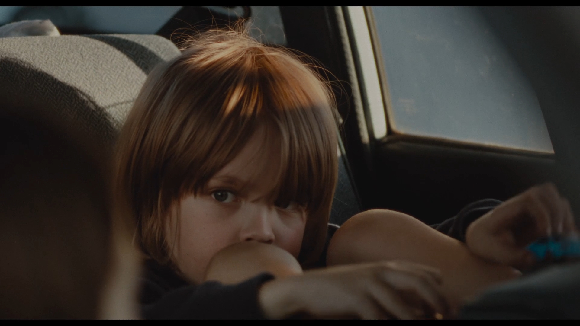 Omaha Review: John Magaro is Amazing in a Dramatic Film That Packs a Wallop Close-up of a young child with light brown hair in a car, looking toward the camera from the backseat with a serious expression.
