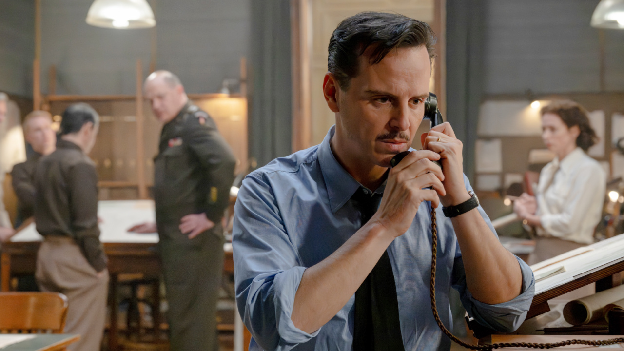 Pressure Review: Brendan Fraser and Andrew Scott are in Top Form for Powerful WWII Drama Man in a blue shirt talks on a corded phone at a busy office desk, with colleagues and a soldier in uniform in the background.