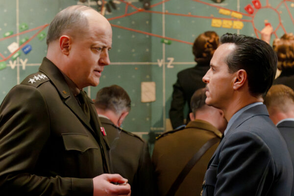 Two military officers in uniform converse in front of a large wall map.