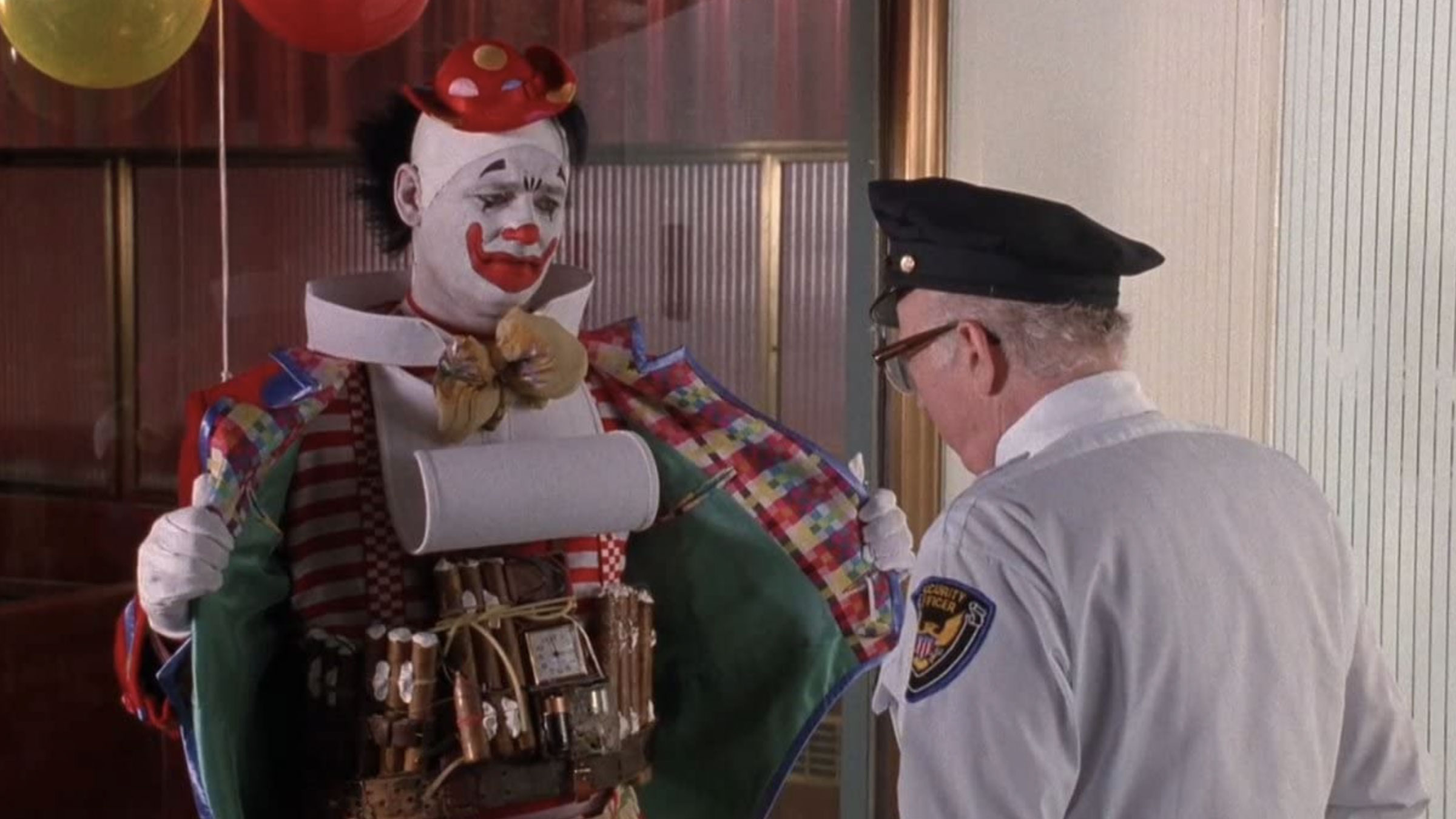 The 12 Greatest Movies Featuring Bill Murray Colorful clown prop with white makeup and red accents being examined by a uniformed security guard in a doorway.