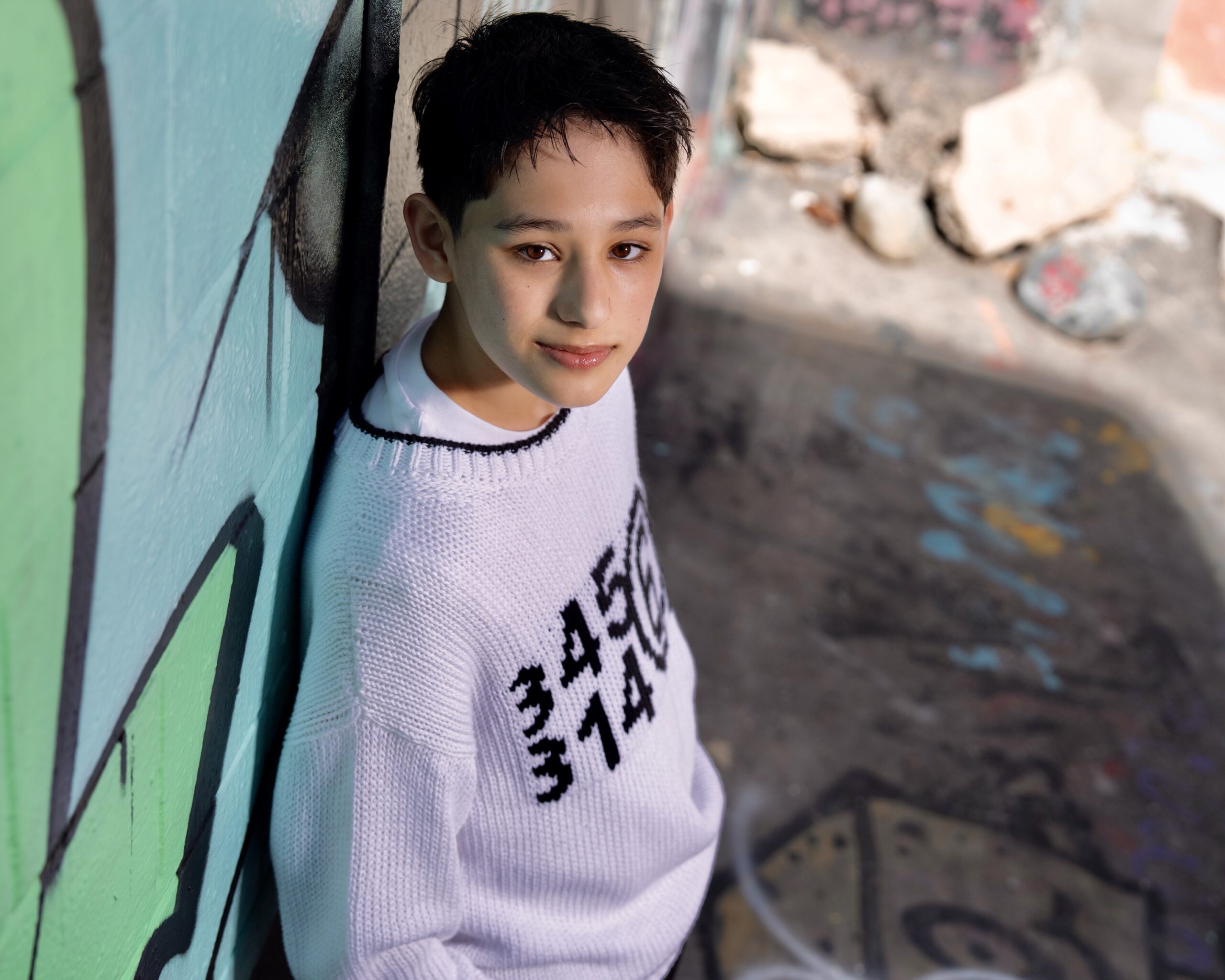 Rain Janjua on Voicing Chase in PAW Patrol: The Dino Movie Actor Rain Janjua, who stars in PAW Patrol: The Dino Movie, poses for a headshot photo, looking up at the camera while leaning against a wall.