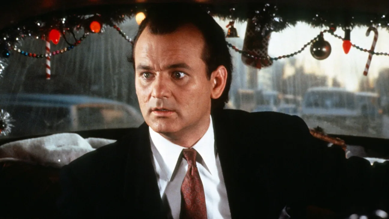 The 12 Greatest Movies Featuring Bill Murray Man in a black suit and red tie sits inside a car decorated with Christmas garlands and lights.