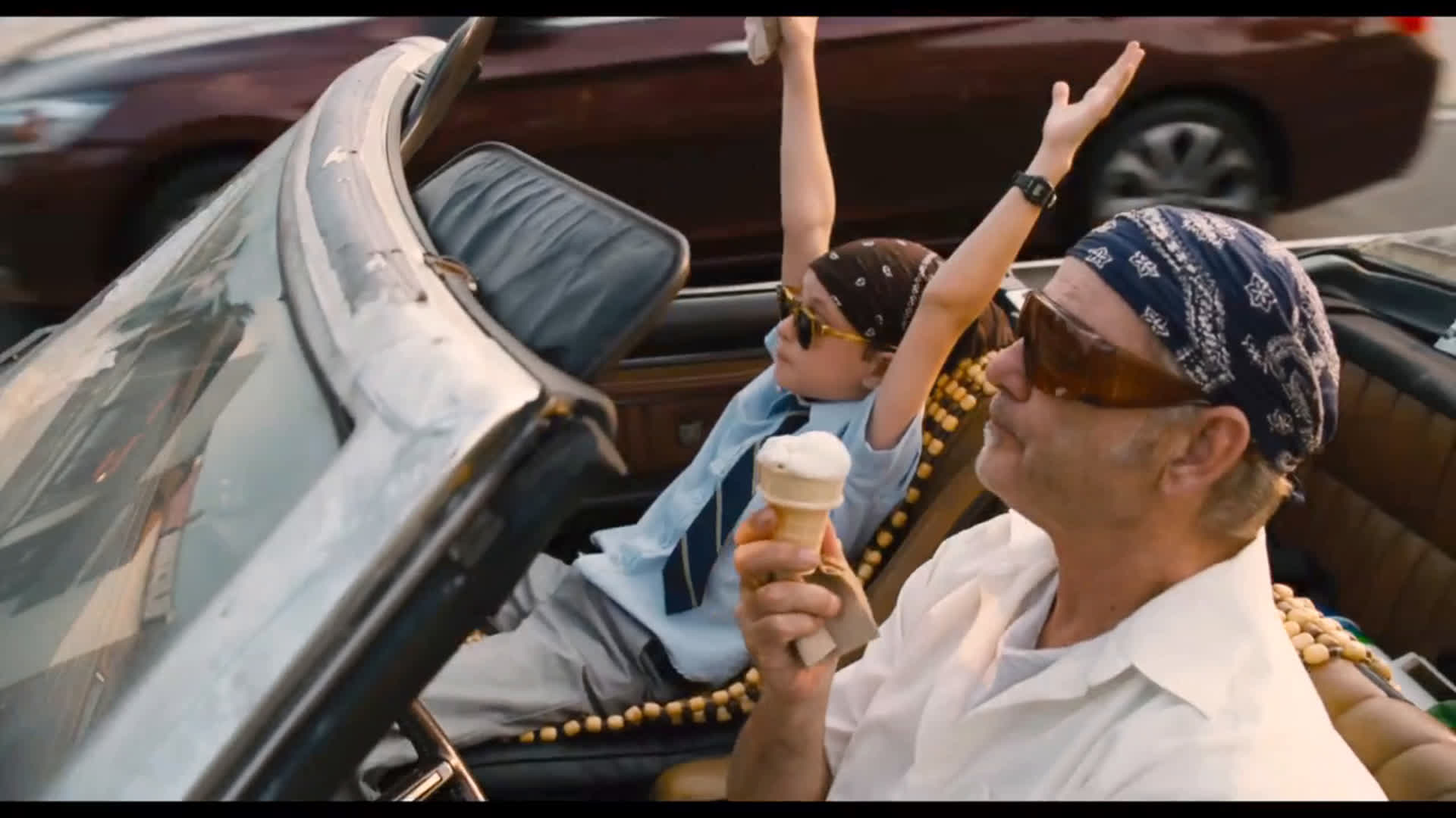 The 12 Greatest Movies Featuring Bill Murray Two people ride in a convertible with the top down; the adult in front wears a blue bandana and sunglasses, holding an ice cream cone while the child raises arms in excitement.