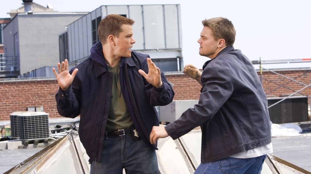 The 12 Best Movies Featuring Matt Damon in a Principal Role Two men in jackets argue on a rooftop, one raising his hands as if deflecting a punch, with industrial equipment in the background.