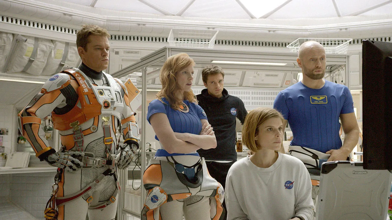 The 12 Best Movies Featuring Matt Damon in a Principal Role A team of astronauts in a bright, futuristic lab gathers around a computer console, one seated woman in a white NASA shirt.