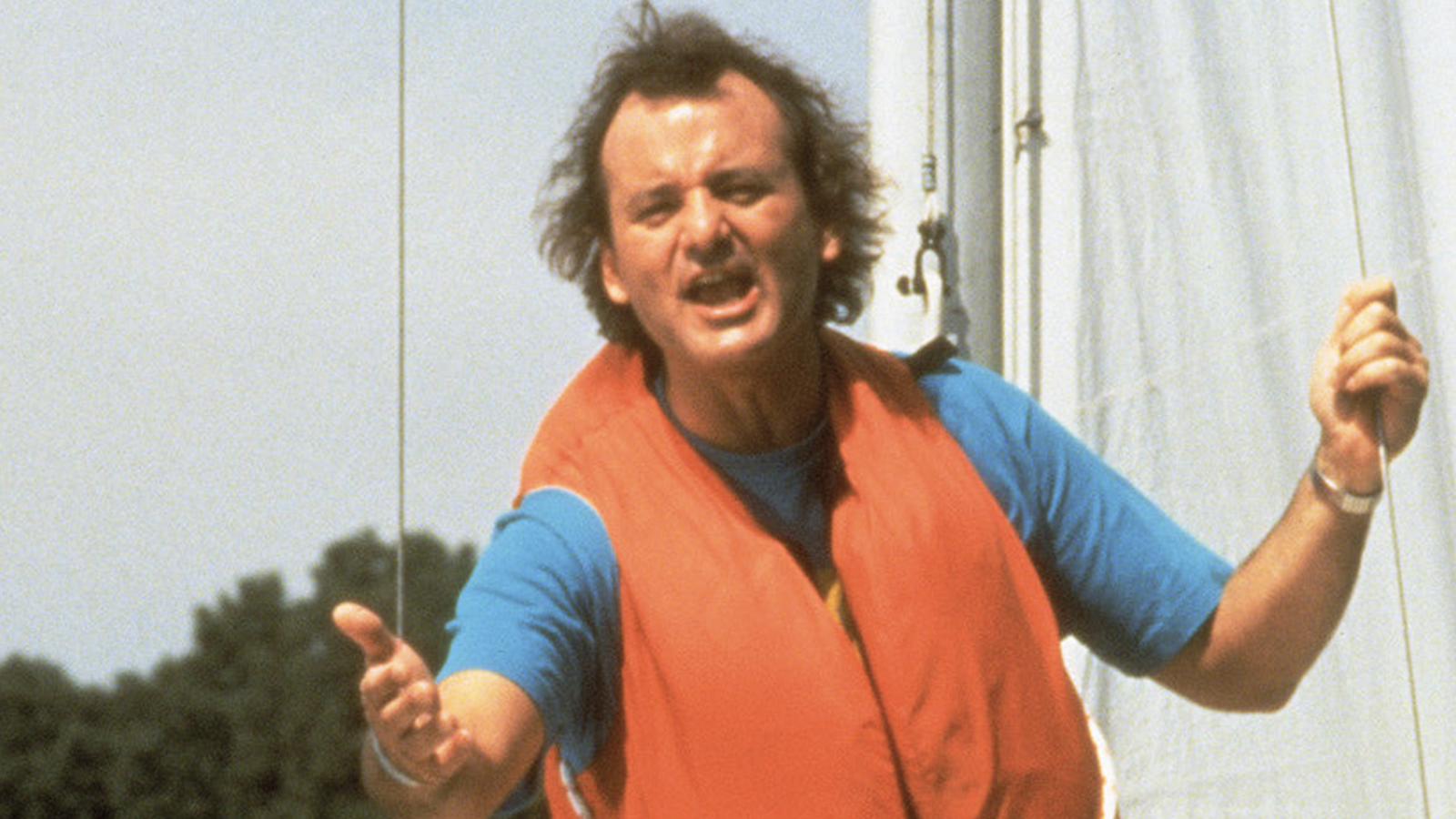 The 12 Greatest Movies Featuring Bill Murray Man in a red life vest on a boat, reaching toward the camera with an open hand.