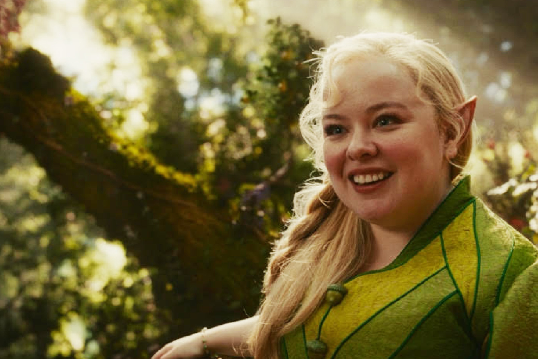 The Magic Faraway Tree Preview: Release Date, Cast, Plot, and More A smiling blonde woman in a green fantasy costume with pointed elf ears outdoors in a sunlit forest.