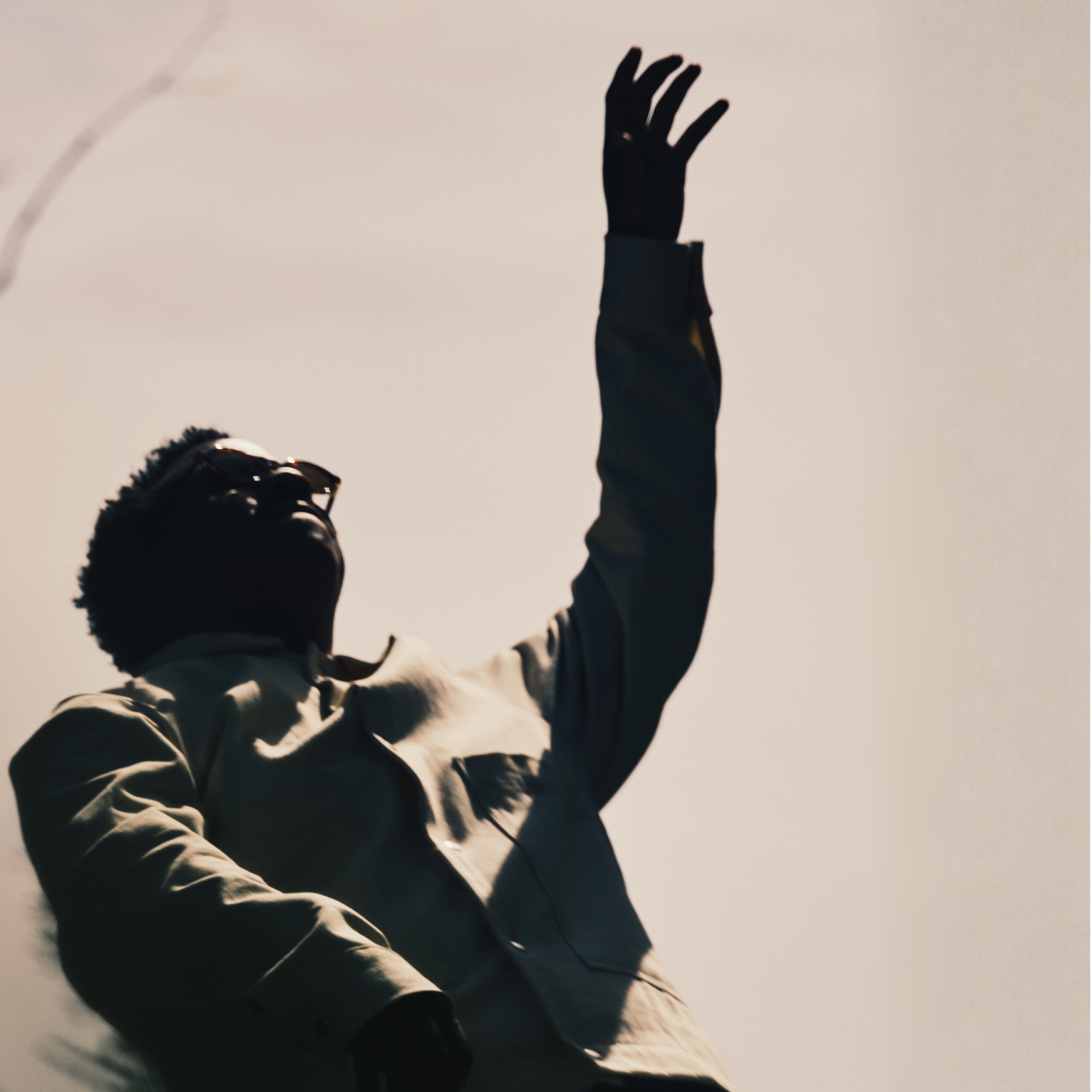 Lee Lewis on New EP, HOWL, Broken Relationships, and Healing Silhouette of a person in a coat raising one arm upward against a pale sky.
