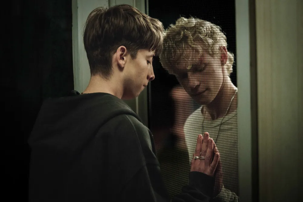 Leviticus Review: A Frightening Horror Movie That Has a Lot on Its Mind Two young men separated by a mesh barrier press their hands to the glass, sharing a tender moment.