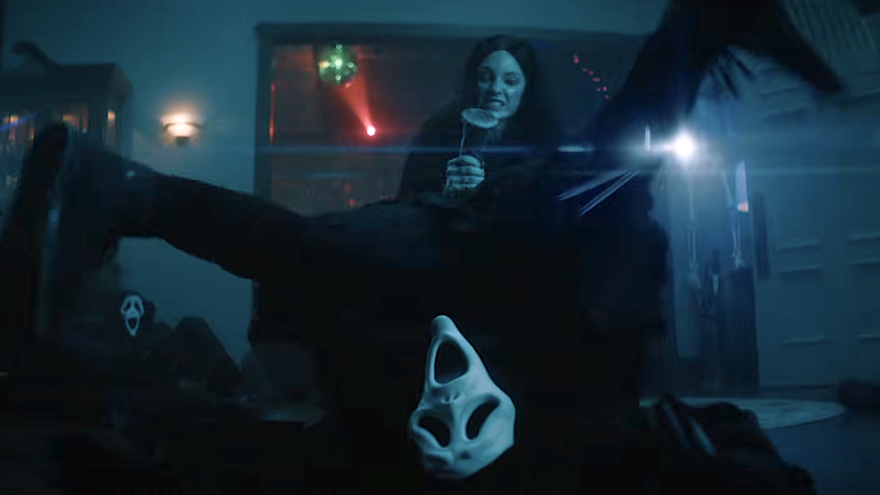 Screenshot - Eulalie Magazine Scary Movie 6 Review: Only a Few Zany Scenes Hit the Comic Bullseye in This Wild Sequel Horror movie still: a white ghost-face mask lies on the floor in a blue-lit room as a woman in the background smiles while holding a drink behind glass.