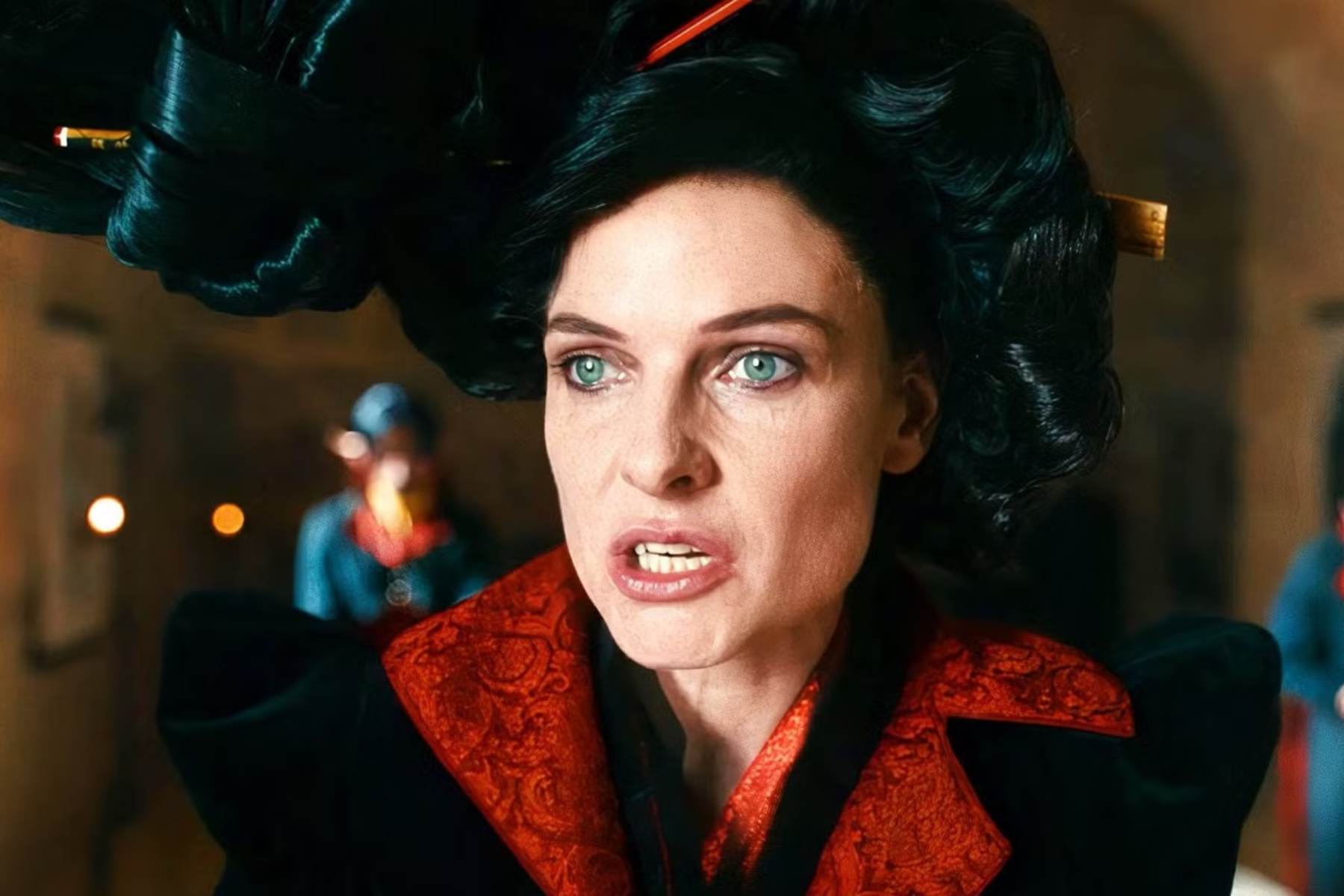 The Magic Faraway Tree Preview: Release Date, Cast, Plot, and More Close-up of a woman with teal eyes and dark hair wearing a black hat and a red brocade jacket, in a dimly lit indoor setting.
