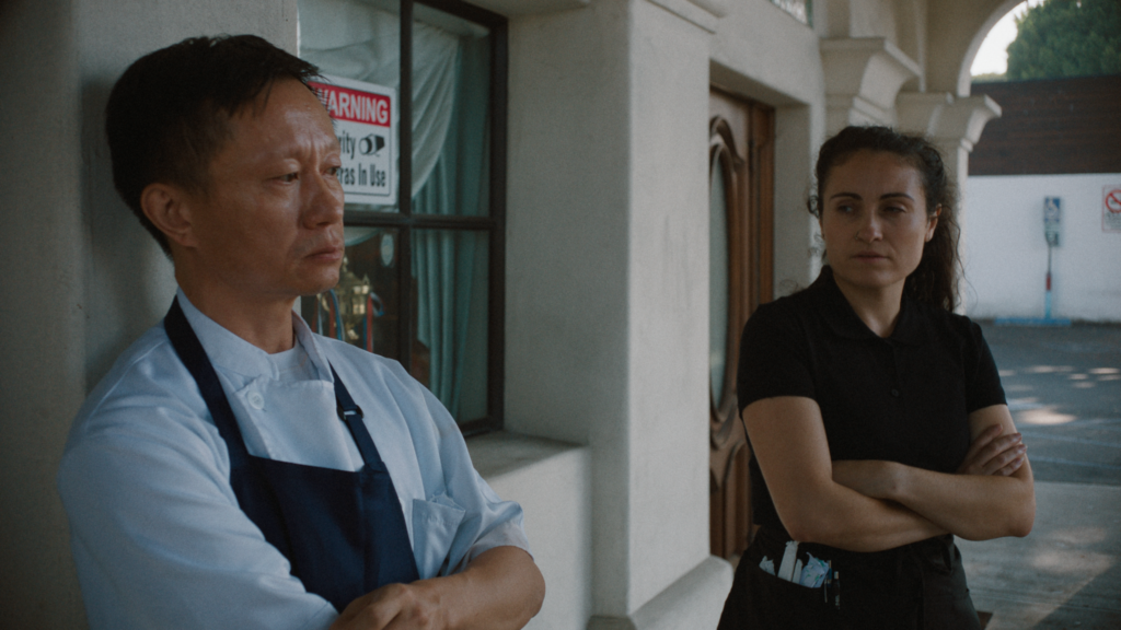 Benny Chen Discusses His Short, HAND Two people stand outside a building, arms crossed: a man in chef whites and apron on the left, a woman in black on the right.