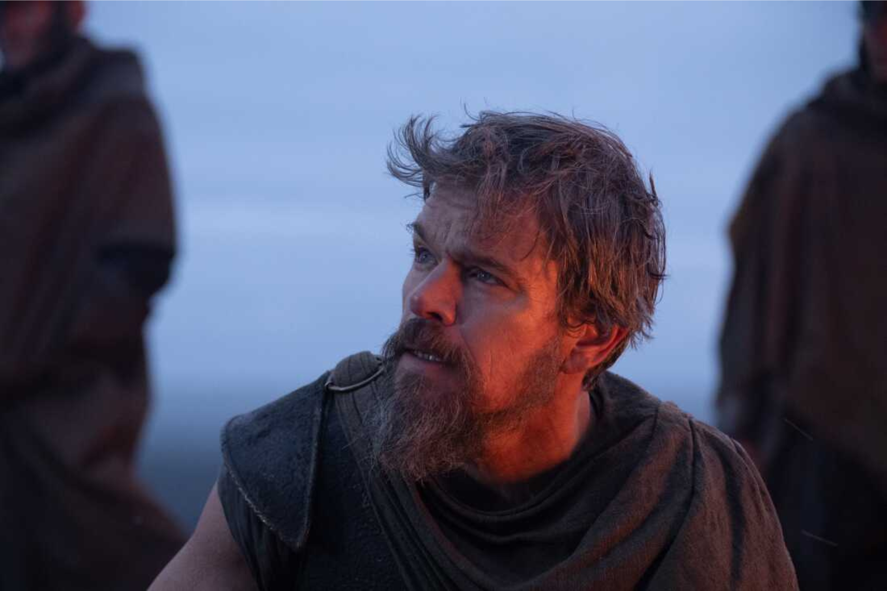 The Odyssey Review: Christopher Nolan Delivers a Modern Masterpiece Bearded man in rugged clothing looks toward someone off-camera as blue hour light glows on his face.