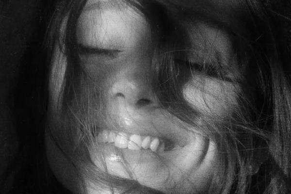 Close-up black-and-white portrait of a person smiling with hair across their face.