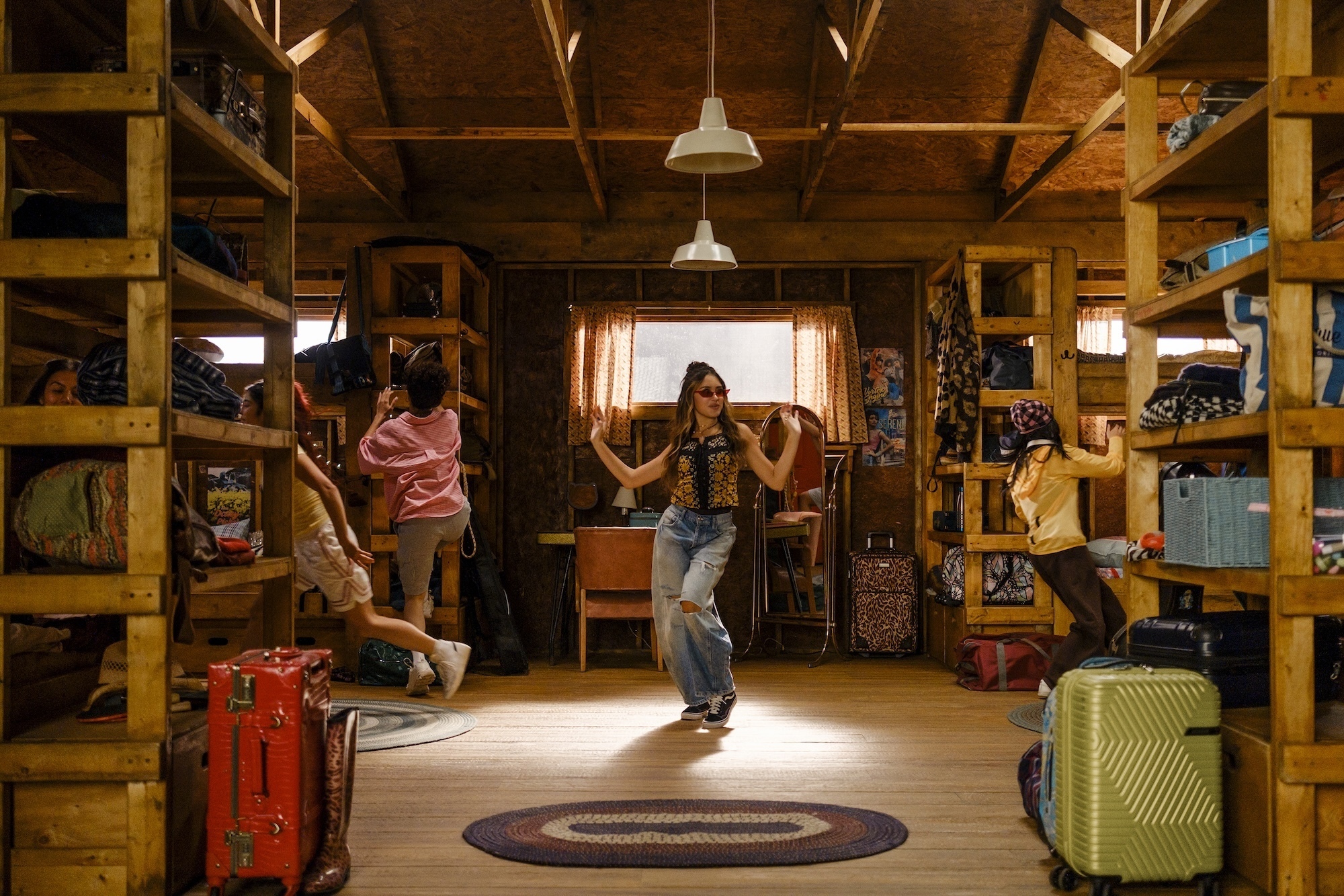Camp Rock 3 Preview: Release Date, Cast, Plot, and More Young woman dancing center in a wooden loft filled with suitcases and shelves of bags and clothes on either side.