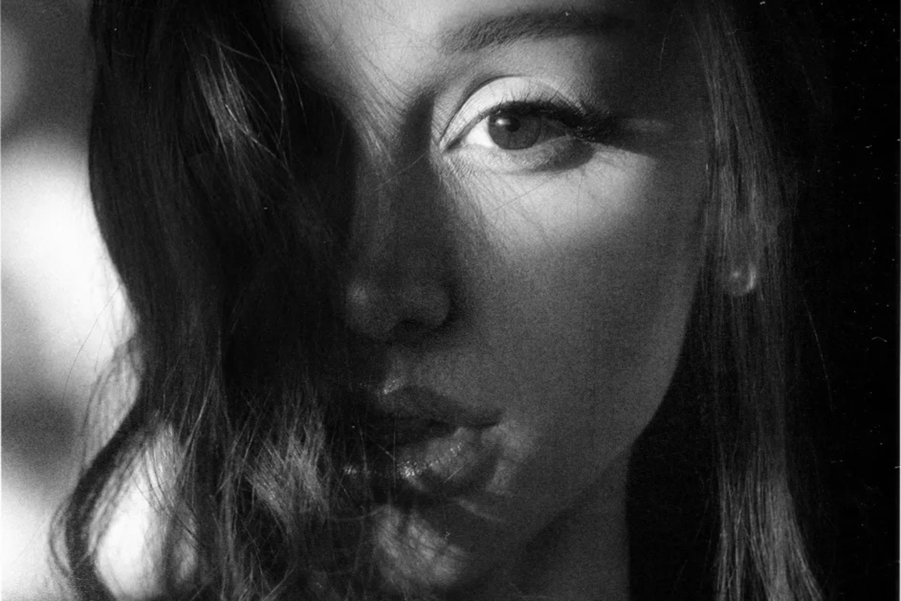 Ariana Grande Finds Power in Reinvention on petal — Album Review Close-up black-and-white portrait of a woman's face, focusing on one visible eye and lips with hair partially covering the cheek.
