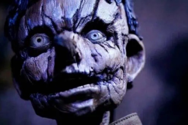 Pinocchio: Unstrung Preview: Release Date, Cast, Plot, and More Close-up of a cracked, grey zombie-like face with bulging blue eyes and dark shadows in blue lighting.