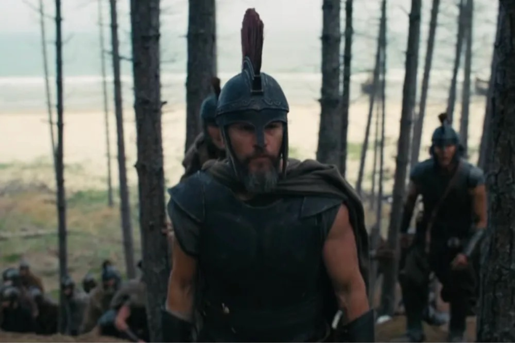 The Odyssey Review: Christopher Nolan Delivers a Modern Masterpiece Armored warrior with a crested helmet leads a marching group through a pine forest, with soldiers in the background.