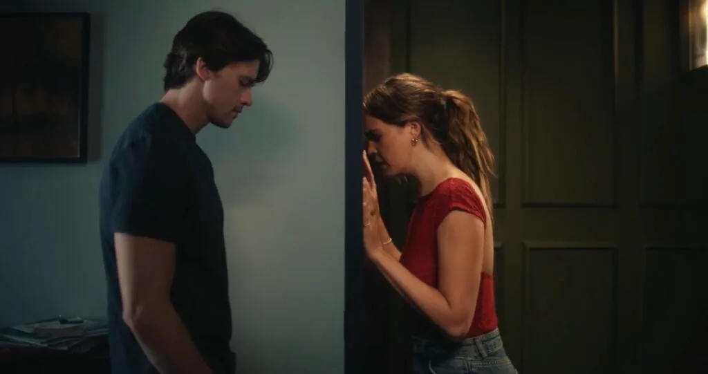 Joel Courtney and Andy Delaney Talk 40 Dates and 40 Nights, Dating Red Flags, and Empathy Two people stand on opposite sides of a narrow doorway wall, heads bowed in a tense moment.
