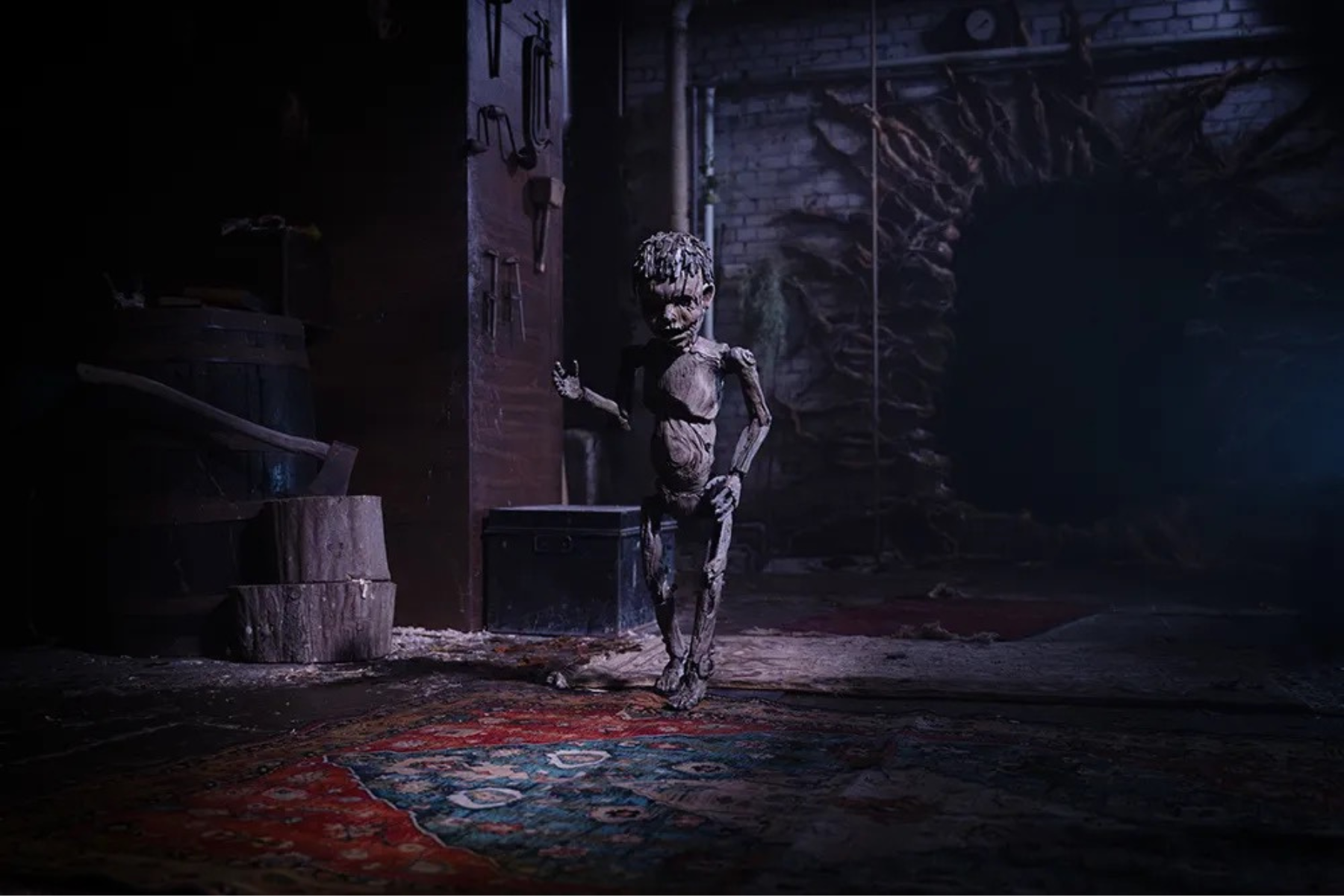 Pinocchio: Unstrung Preview: Release Date, Cast, Plot, and More A pale, ragged humanoid figure stands in a dark basement, with tools on the wall and a red patterned rug on the floor.
