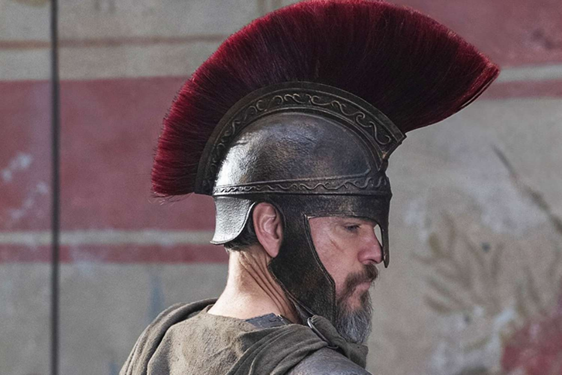 The Odyssey Review: Christopher Nolan Delivers a Modern Masterpiece Side profile of a man wearing a metal helmet with a burgundy plume, looking left.