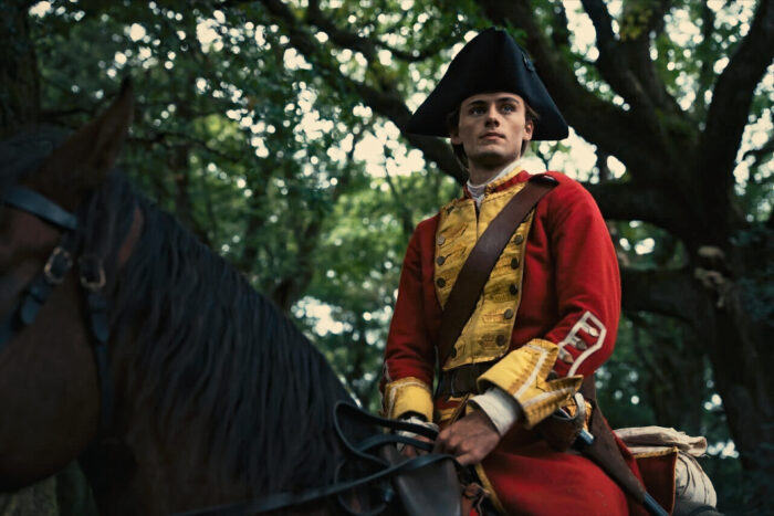 Young Washington Preview: Release Date, Cast, Plot, and More Man dressed in a red colonial-era uniform with a black tricorn hat sits upright on a horse in a forest.