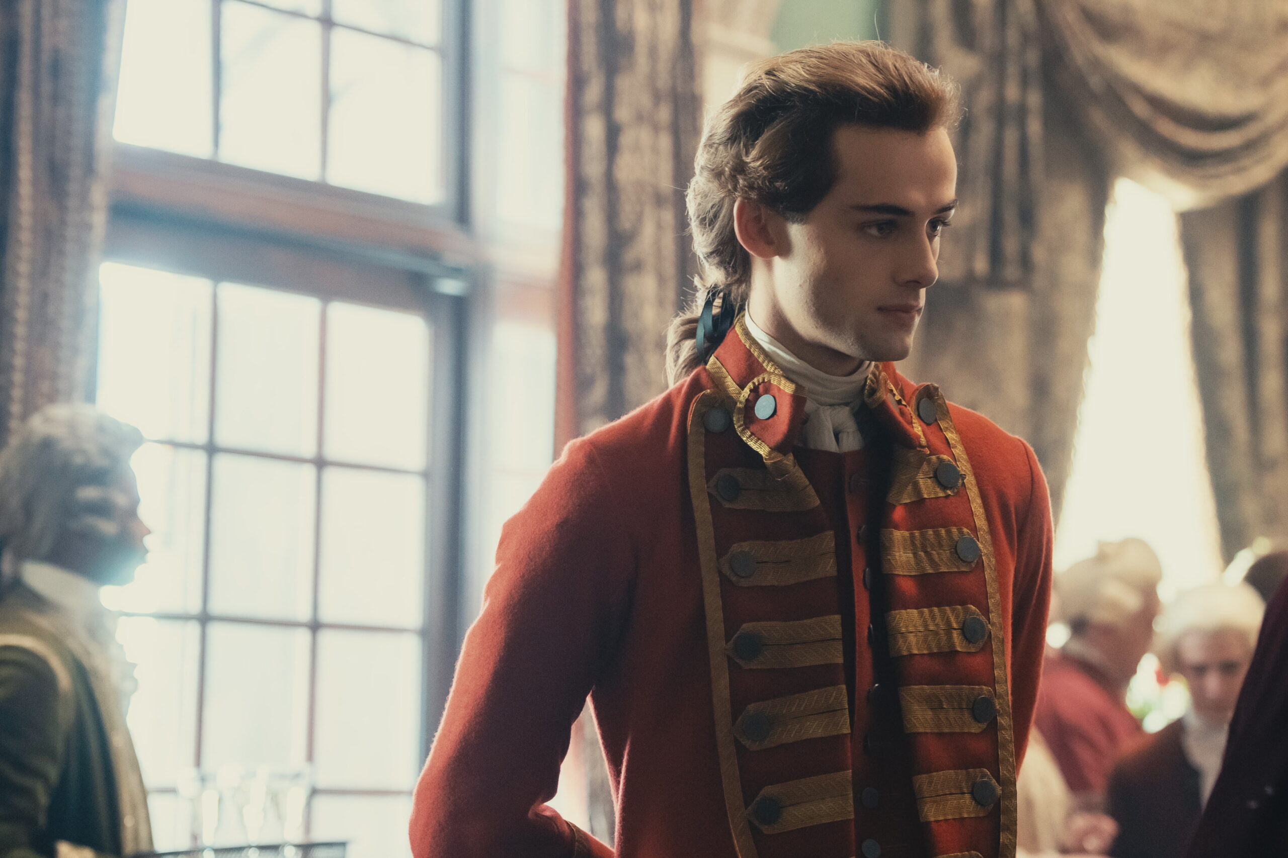 Young Washington Preview: Release Date, Cast, Plot, and More Man wearing a vintage red coat with gold braid, indoors near large windows, looking to the right.