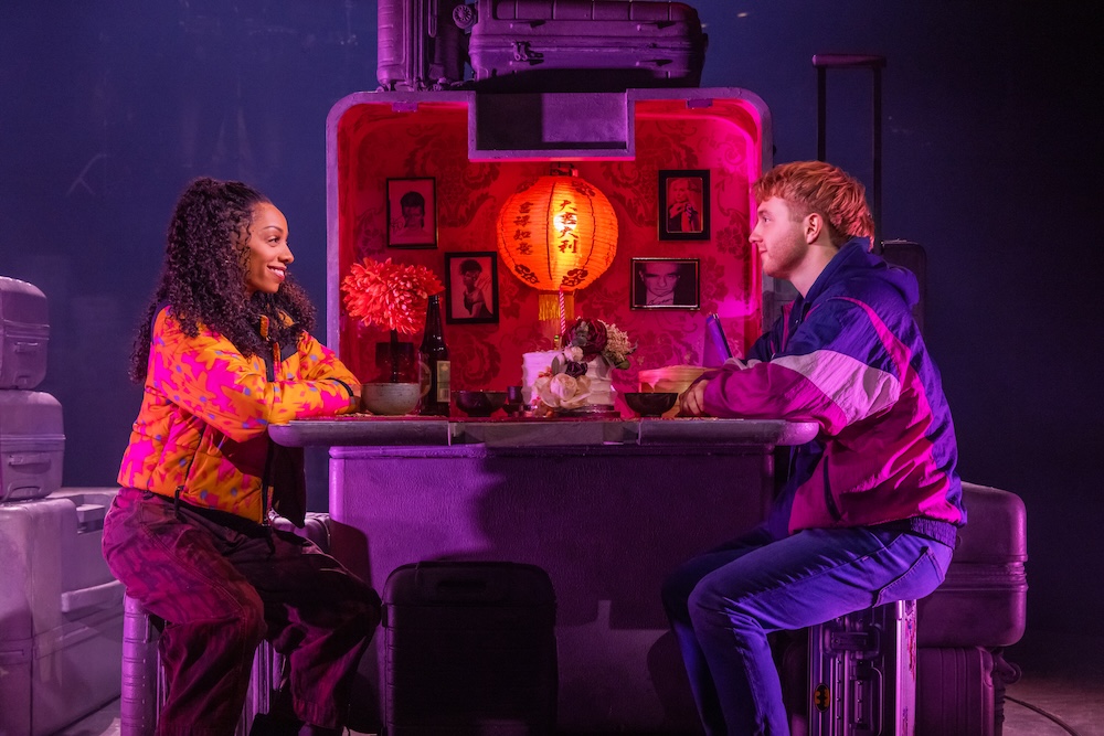 Two Strangers (Carry a Cake Across New York) Review: Relatable Situations and Memorable Characters Make for a Fun Musical Two people sit across from each other at a neon-lit bar or counter, chatting over drinks and snacks under a red lantern backdrop.