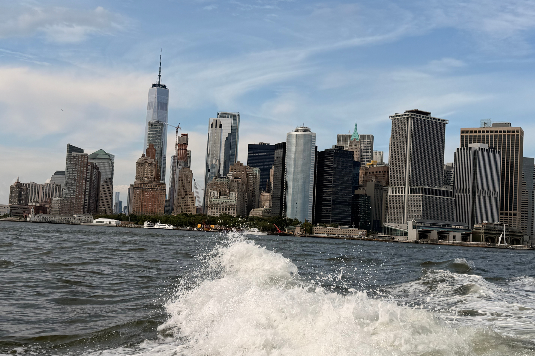 NYC by Sea - Eulalie Magazine First Time in New York City? Here’s Everything You Need to Know Before You Go! New York City skyline along the harbor with waves splashing in the foreground under a blue sky, centered on tall skyscrapers a:0.75