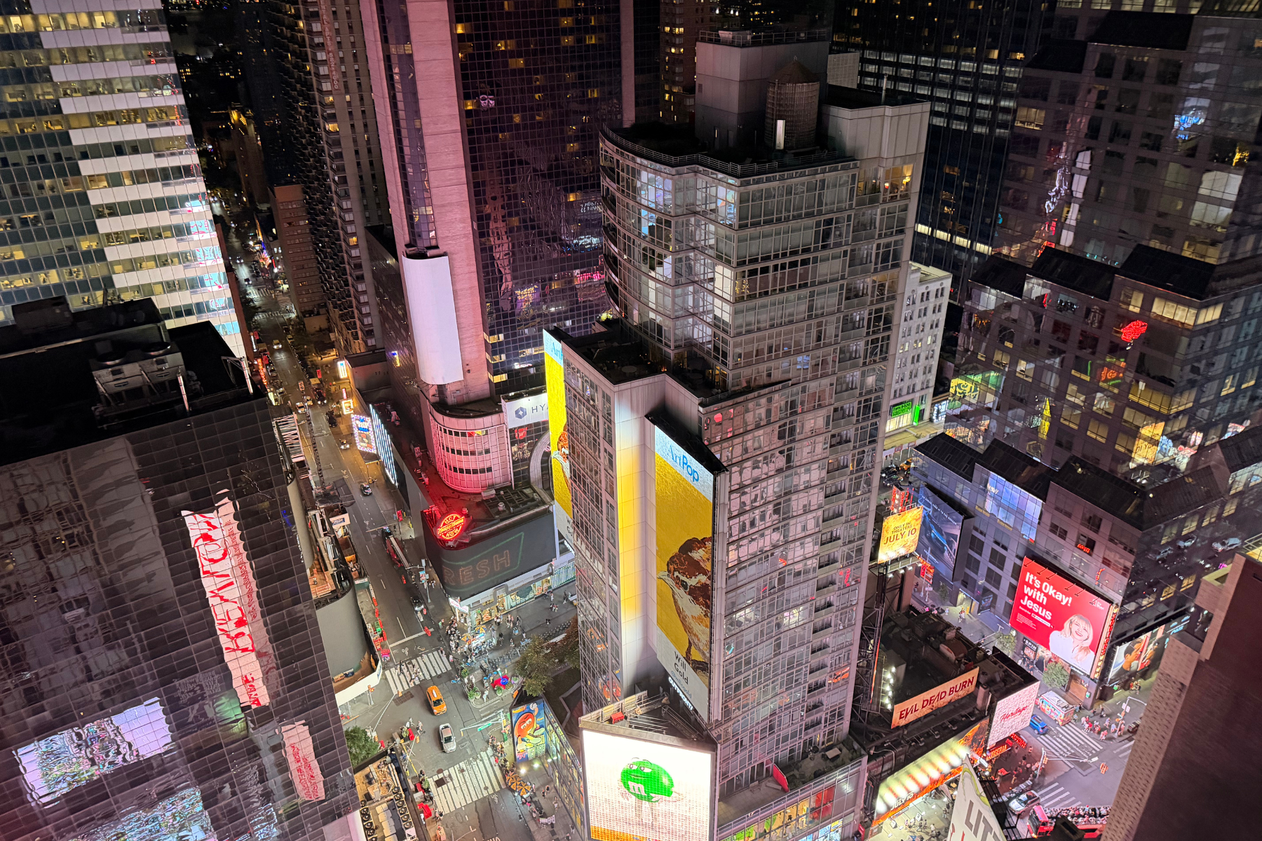 Times Square NYC - Eulalie Magazine First Time in New York City? Here’s Everything You Need to Know Before You Go! Nighttime aerial view of Times Square with illuminated billboards and tall buildings forming a dense cityscape.
