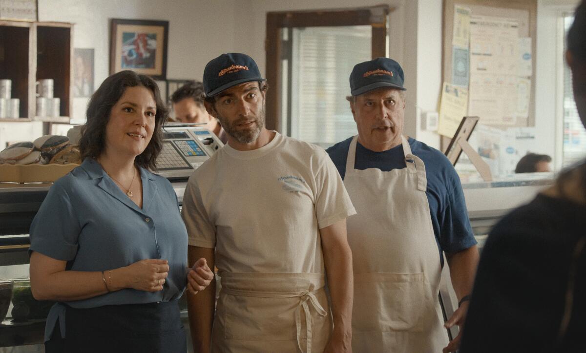 Don’t Say Good Luck Review: Sunny Sandler is Solid Gold in This Slice of Life Drama Three bakery staff stand at a counter, two men in aprons and caps beside a woman in a blue shirt, smiling at customers.