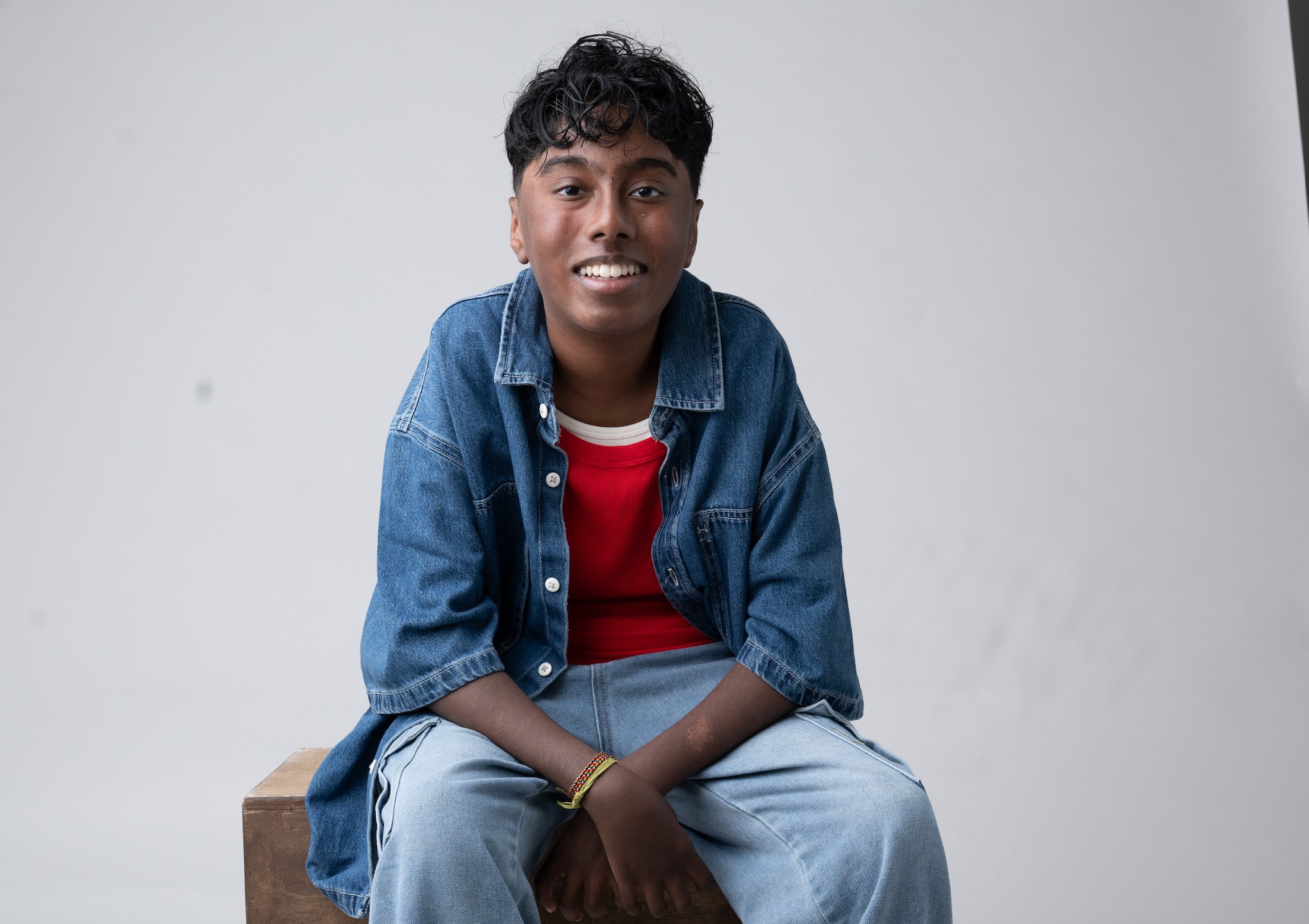Nylan Parthipan Talks PAW Patrol: The Dino Movie Actor Nylan Parthipan smiles for a headshot while sitting in front of a white background.