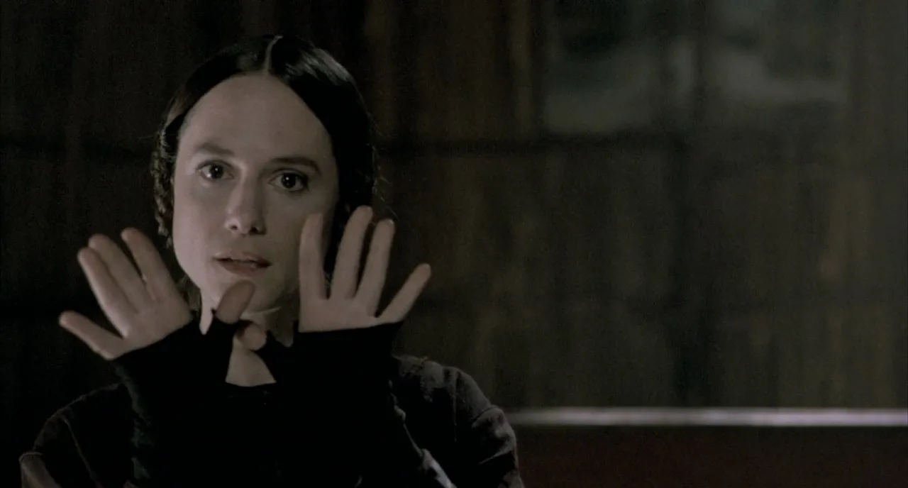The Piano 4K Restoration Review: Holly Hunter’s Performance Ages Like Fine Wine in a Sweeping Film Woman in a dark room raises hands in a surrender gesture, looking anxious.